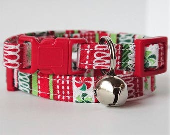 May include: Red and green Christmas-themed cat collar with a bell. The collar is made of fabric with a white background and features a red buckle.