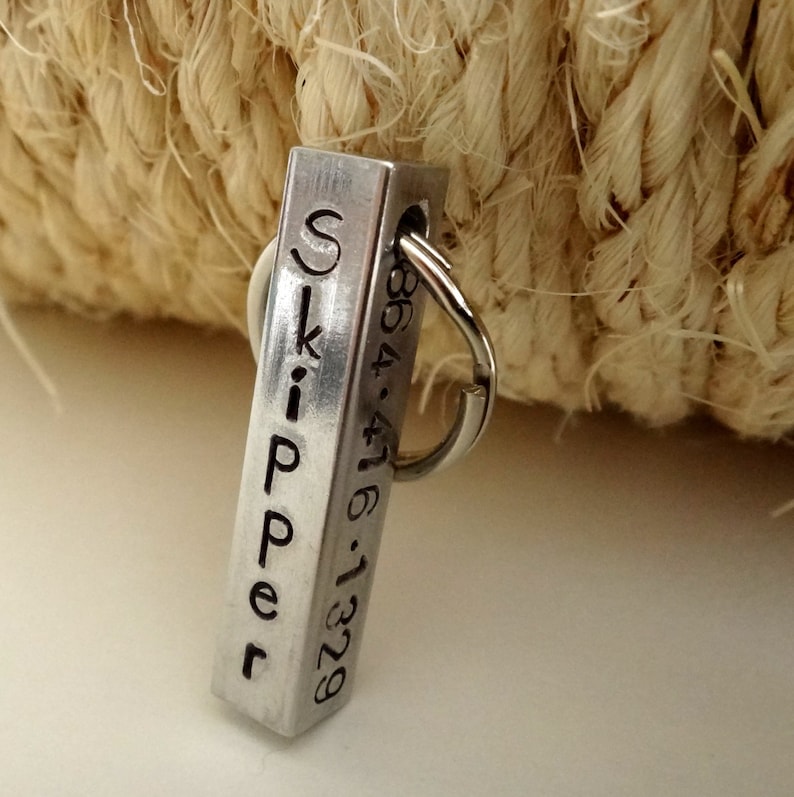 May include: Silver metal keychain with a rectangular tag engraved with the name "Skipper" and the phone number "864-476-1329".