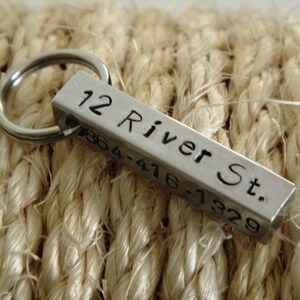 May include: Silver key chain with a rectangular tag engraved with "12 River St. 0864-416-7329".