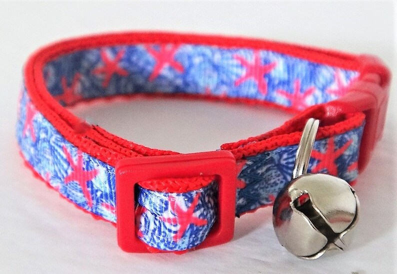 Peut inclure: Collier pour chat rouge et bleu avec une clochette argent&eacute;e. Le collier a une boucle rouge et un motif bleu et blanc avec des &eacute;toiles de mer rouges.