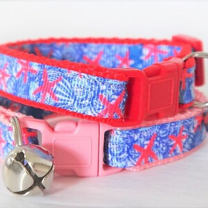 Peut inclure: Deux colliers pour chat avec un motif de coquillages bleu et rouge. Les colliers ont une boucle rouge et rose et une clochette argent&eacute;e sur chacun.