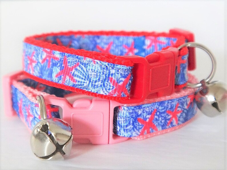 Peut inclure: Deux colliers pour chat avec un motif de coquillages bleu et rouge. Les colliers ont une boucle rouge et rose et une clochette argent&eacute;e sur chacun.