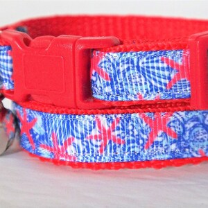Peut inclure: Collier de chat rouge avec un ruban &agrave; motif bleu et blanc orn&eacute; d'&eacute;toiles de mer roses. Le collier a une boucle rouge et une clochette argent&eacute;e.
