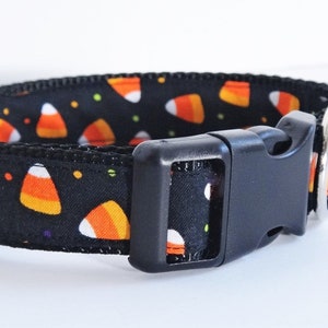 May include: Black dog collar with a candy corn pattern. The collar has a black plastic buckle and a silver metal D-ring.