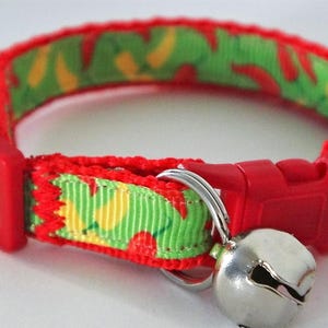 Może przedstawiać: Czerwono-zielony obroża dla kota z dzwoneczkiem. Obroża ma ż&oacute;łto-zielony wz&oacute;r z czerwonymi papryczkami chili.