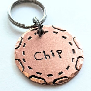 May include: Copper dog tag with a rounded, textured edge and the name "Chip" engraved in the center.