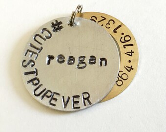 May include: Silver dog tag with the text "CUTEST PUP EVER" and the name "Reagan" engraved on it. A gold tag with the numbers "1.9.47.19.82" is attached to the silver tag.