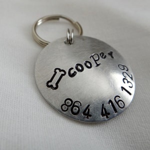 K&ouml;nnte beinhalten: Silbernes Hundehalsband mit einem Knochen und dem Namen "Cooper" eingraviert. Das Halsband hat auch die Telefonnummer 864 416 1329 eingraviert.