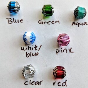 May include: Assortment of 10 glass beads in various colors, including blue, green, aqua, white/blue, pink, clear, and red. Each bead has a silver-toned metal trim.
