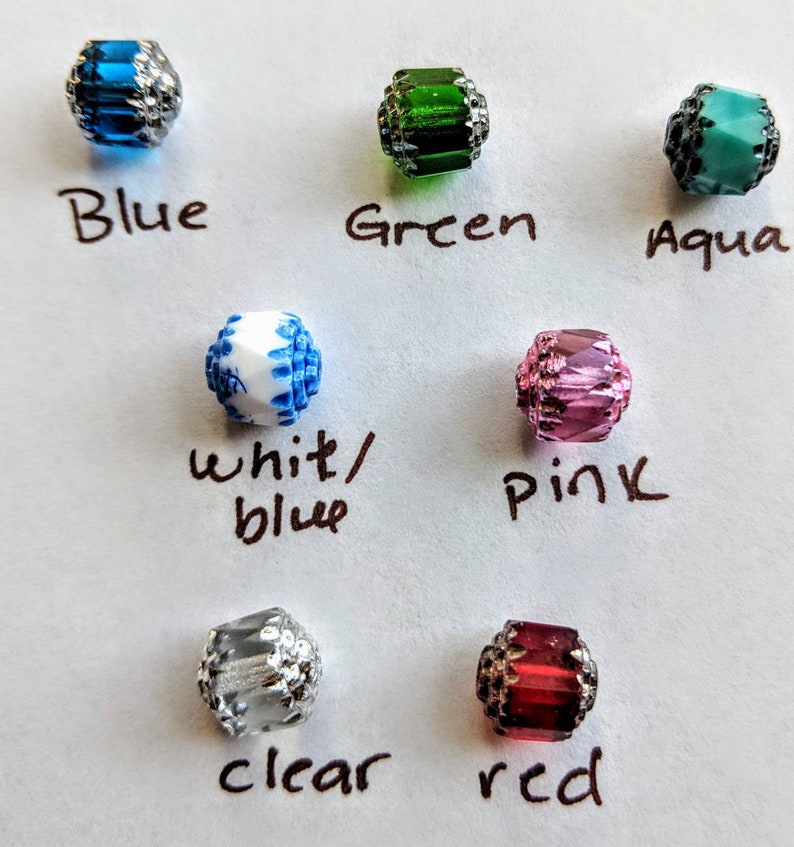 May include: Assortment of 10 glass beads in various colors, including blue, green, aqua, white/blue, pink, clear, and red. Each bead has a silver-toned metal trim.