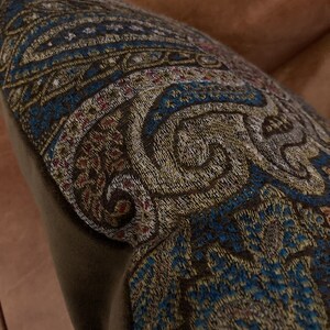 Puede incluir: Una almohada de tiro de color marr&oacute;n y azul con un bordado intrincado. La almohada est&aacute; hecha de una tela suave y mullida y tiene un brillo sutil.