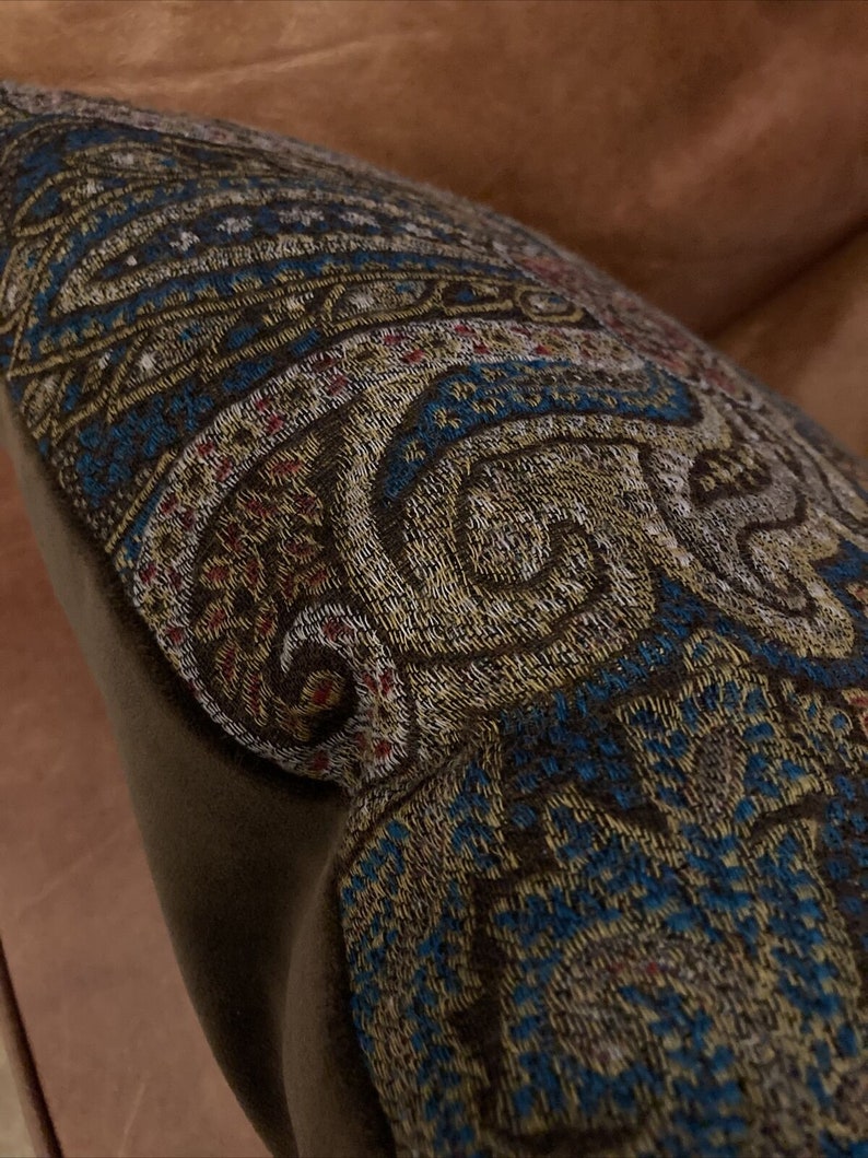 Puede incluir: Una almohada de tiro de color marr&oacute;n y azul con un bordado intrincado. La almohada est&aacute; hecha de una tela suave y mullida y tiene un brillo sutil.