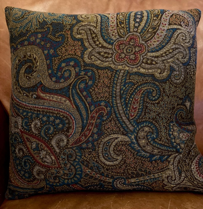 Puede incluir: Una almohada decorativa con un patr&oacute;n de paisley en tonos de marr&oacute;n, azul verdoso, dorado y rojo.