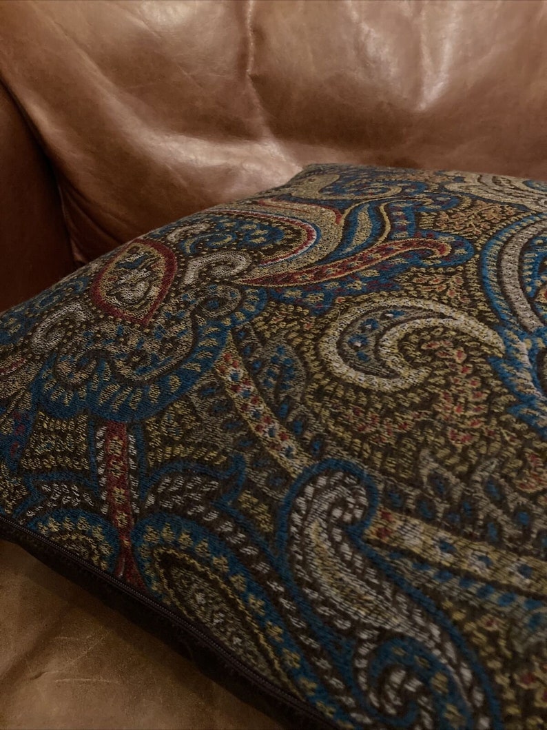 Puede incluir: Una almohada de tiro de color marr&oacute;n, azul y dorado con un patr&oacute;n de paisley y una cremallera marr&oacute;n oscuro.