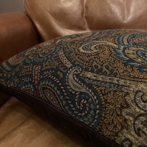 Puede incluir: Un sill&oacute;n de cuero marr&oacute;n con un coj&iacute;n de decoraci&oacute;n con estampado paisley. El coj&iacute;n tiene una cremallera marr&oacute;n oscuro y un borde marr&oacute;n oscuro.