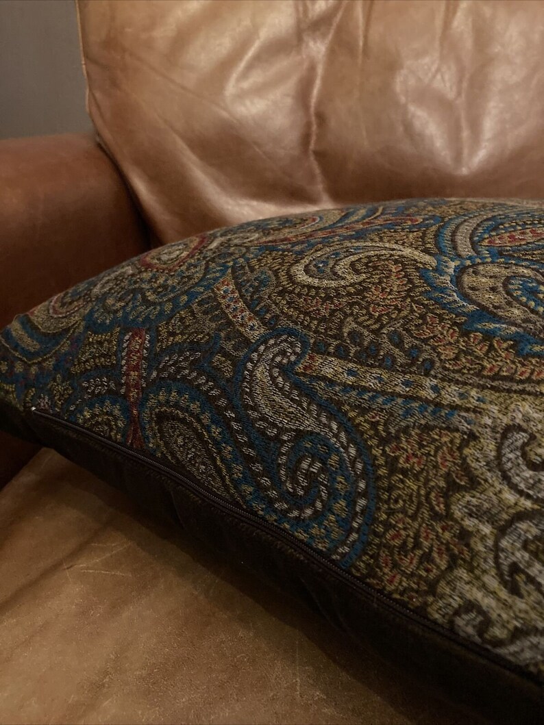Puede incluir: Un sill&oacute;n de cuero marr&oacute;n con un coj&iacute;n de decoraci&oacute;n con estampado paisley. El coj&iacute;n tiene una cremallera marr&oacute;n oscuro y un borde marr&oacute;n oscuro.