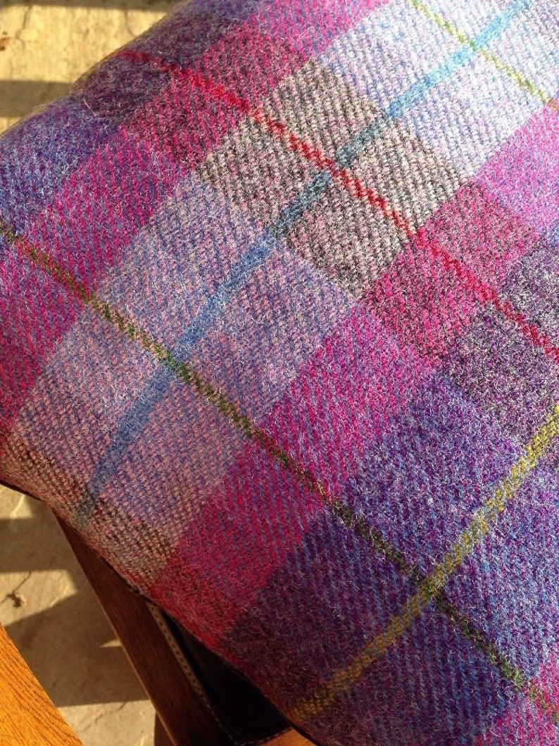 May include: Close-up of a cushion with a vibrant plaid pattern. The fabric features a mix of pink, purple, blue, and yellow lines, creating a colorful and textured design. The cushion is likely made of a woven material, possibly wool or a similar fabric.
