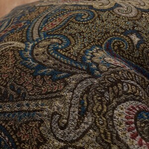 Puede incluir: Primer plano de una tela de color marr&oacute;n, azul y crema con estampado paisley. La tela tiene un aspecto texturizado y tejido.