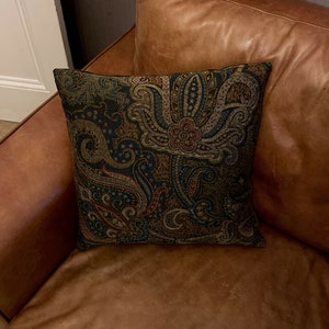 Puede incluir: Un sof&aacute; de cuero marr&oacute;n con un coj&iacute;n con estampado paisley. El coj&iacute;n tiene un fondo azul oscuro con dise&ntilde;os paisley marrones, rojos y dorados.