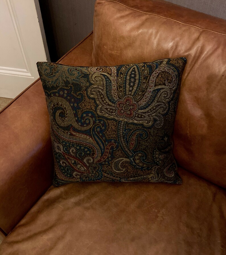 Puede incluir: Un sof&aacute; de cuero marr&oacute;n con un coj&iacute;n con estampado paisley. El coj&iacute;n tiene un fondo azul oscuro con dise&ntilde;os paisley marrones, rojos y dorados.