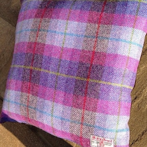 May include: Square pillow with a purple, pink, and white plaid pattern. The pillow has a Harris Tweed label in the lower right corner. The plaid design includes red, yellow, and blue accent lines.