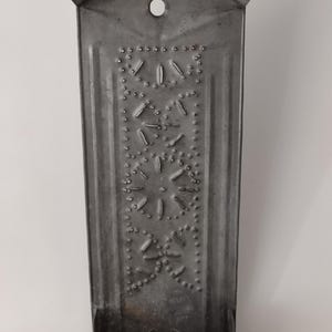 May include: A vintage, gray metal candle holder with a scalloped top and a decorative punched star design. The candle holder has a cylindrical base and a small hole near the top. A rustic, antique home decor item.