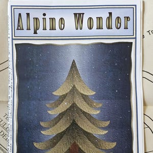 May include: A pattern titled "Alpine Wonder" featuring a stylized tree design. The tree is depicted in shades of green and brown against a dark blue starry sky. The pattern measures 35" x 43".