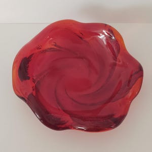 May include: A red glass bowl with a swirl design. The bowl has a wavy edge and is made of clear glass with a red tint.