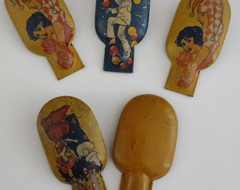 May include: Five vintage tin toys shaped like a teardrop. Each toy has a different image. One toy has a clown juggling balls, another has a woman with a jester hat, another has a woman with a jester hat, another has a clown with a red hat, and the last one is plain.