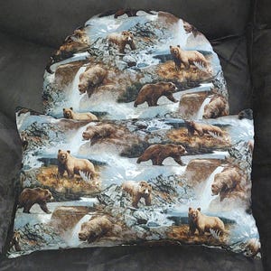 May include: A decorative pillow and headrest set featuring a repeating pattern of brown bears in a mountain landscape with waterfalls. The fabric has a light blue and brown color scheme.