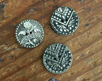 May include: Three silver metal buttons with intricate floral designs. The buttons have a raised, textured surface and a circular shape.