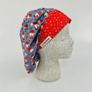 May include: A blue and red scrub hat with a gnome pattern on one side and a snowflake pattern on the other. The hat has a label that says "KlinKaps".