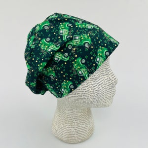 Peut inclure: Un bonnet de travail en tissu vert et or avec un motif de camions verts et de trèfles. Les camions portent l'inscription "Happy St. Patrick's Day".