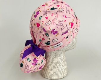 Puede incluir: Un gorro quirúrgico rosa con un lazo morado, estampado con ilustraciones de temática médica y el texto "registered silly goose". El gorro tiene un soporte para cola de caballo y está diseñado para profesionales médicos.