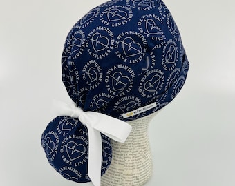 Peut inclure: Casquette de chirurgien bleu marine avec un motif de cœur et de battement de cœur blancs, entouré du texte "IT'S A BEAUTIFUL DAY TO SAVE LIVES". Un ruban blanc est noué à l'arrière. Destiné aux professionnels de la santé.