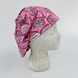 May include: Pink surgical scrub hat with a colorful pattern of hearts and circles. The hat has a label that says "KimKaps".