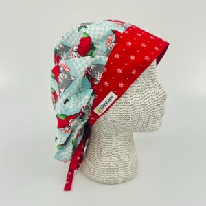 May include: A blue and red surgical scrub hat with a Christmas cat print. The hat has a tie and the text "KimKeps" is on the hat.