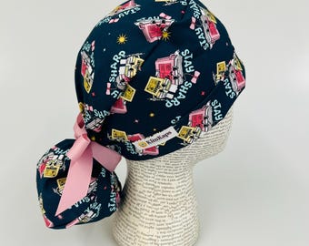 Puede incluir: Un gorro quirúrgico azul marino con un lazo rosa y las palabras "Stay Sharp" impresas. El gorro presenta un patrón repetido de gráficos médicos rosas y amarillos y estrellas.