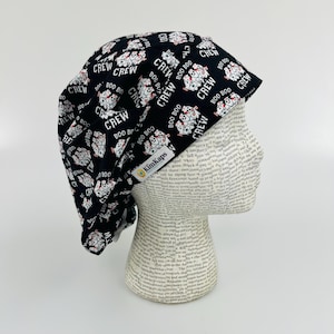 May include: Black scrub hat with a white print of dogs and the words "Boo Boo Crew". The hat is on a white mannequin head.