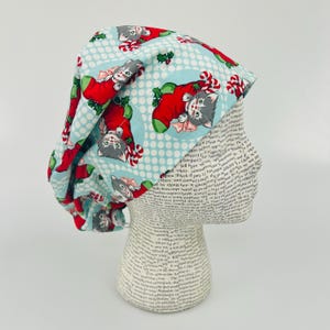 May include: A blue and white patterned scrub hat with a repeating pattern of kittens wearing Santa hats and candy canes.