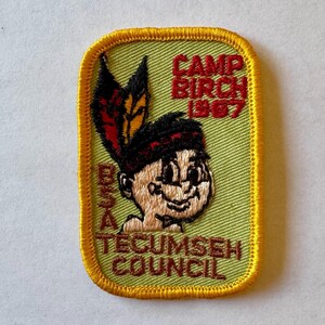 May include: A green and yellow embroidered patch with a cartoon image of a Native American boy wearing a headdress. The patch says "Camp Birch 1967" and "BSA Tecumseh Council".