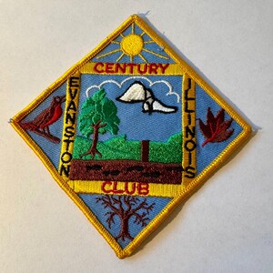 Op de afbeelding: Een blauwe ruitvormige patch met een gele rand. De patch heeft een zon, een vogel, een boom, een vlinder, een blad en de tekst "Century Evanston Illinois Club".