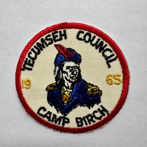 May include: Circular patch with a red border and the words "TECUMSEH COUNCIL" and "CAMP BIRCH" in black. The patch features an illustration of a Native American chief in blue and gold, with a red and black feather. The numbers "19" and "65" are in gold.