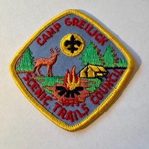 Peut inclure: Un écusson brodé bleu et jaune avec le texte "Camp Greilick Scenic Trails Council" et une représentation d'un feu de camp, d'une tente, d'un cerf et d'une fleur de lys.