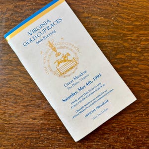 May include: A vintage Virginia Gold Cup Races program from 1991. The cover is white with blue and gold text, featuring a horse racing graphic. The program is dedicated to the forces in the Persian Gulf War.