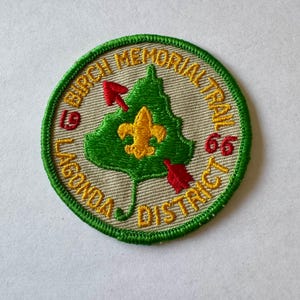 May include: A green and beige embroidered patch with the text "Birch Memorial Trail 66 Lagonda District" and a green tree with a yellow fleur-de-lis in the center.