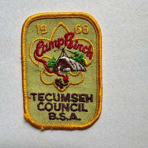 Könnte beinhalten: Ein rechteckiger Aufnäher mit hellgrünem Hintergrund und goldenem Rand. Der Aufnäher zeigt die Worte "Camp Birch" in roter Schrift, eine Zeltillustration und den Text "Tecumseh Council B.S.A." in Braun.