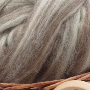 May include: A close-up of a bundle of light brown and white wool roving. The roving is soft and fluffy, and it is perfect for spinning or felting.