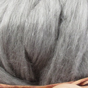 May include: Close-up of a mass of gray wool roving, showing the soft, textured fibers. The wool is a solid, neutral color, ideal for various crafting projects. The roving is presented in a woven basket.
