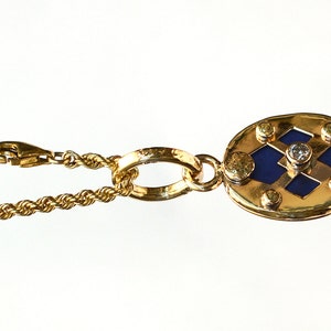 May include: A gold necklace with a pendant featuring a blue and gold geometric design with a small diamond in the center.